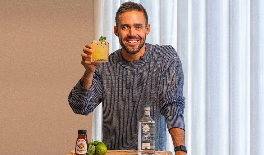 A photo of Spencer Matthews standing and smiling at the camera, holding a mocktail made with an alcohol-free spirit from his company CleanCo.