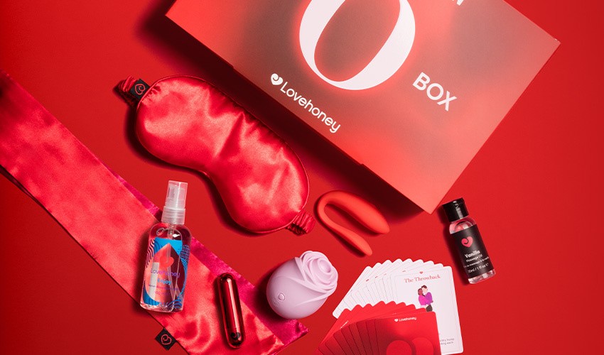 The Lovehoney x Cosmopolitan O Box showing sexual wellness products such as a pastel pink rose toy spilling onto a vibrant red background.