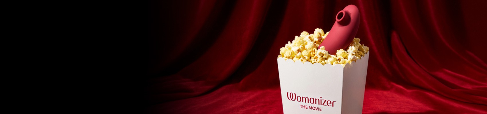 A red curtain background with a photograph of a popcorn bucket filled with popcorn and a Womanizer toy inside.