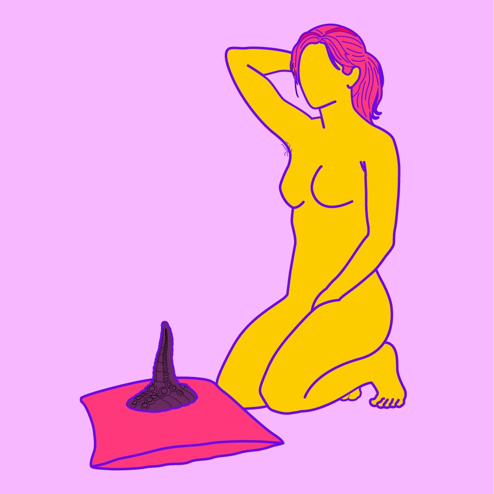 A naked illustrated woman knelt on the floor and touching herself, with a dildo propped on a pillow in front of her.