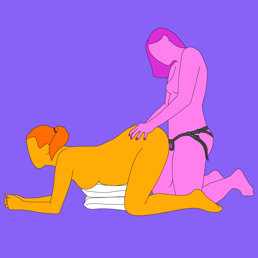 A naked illustrated couple in a doggy style position. One is on their knees and resting on some pillows and the other is behind, wearing a strap-on.