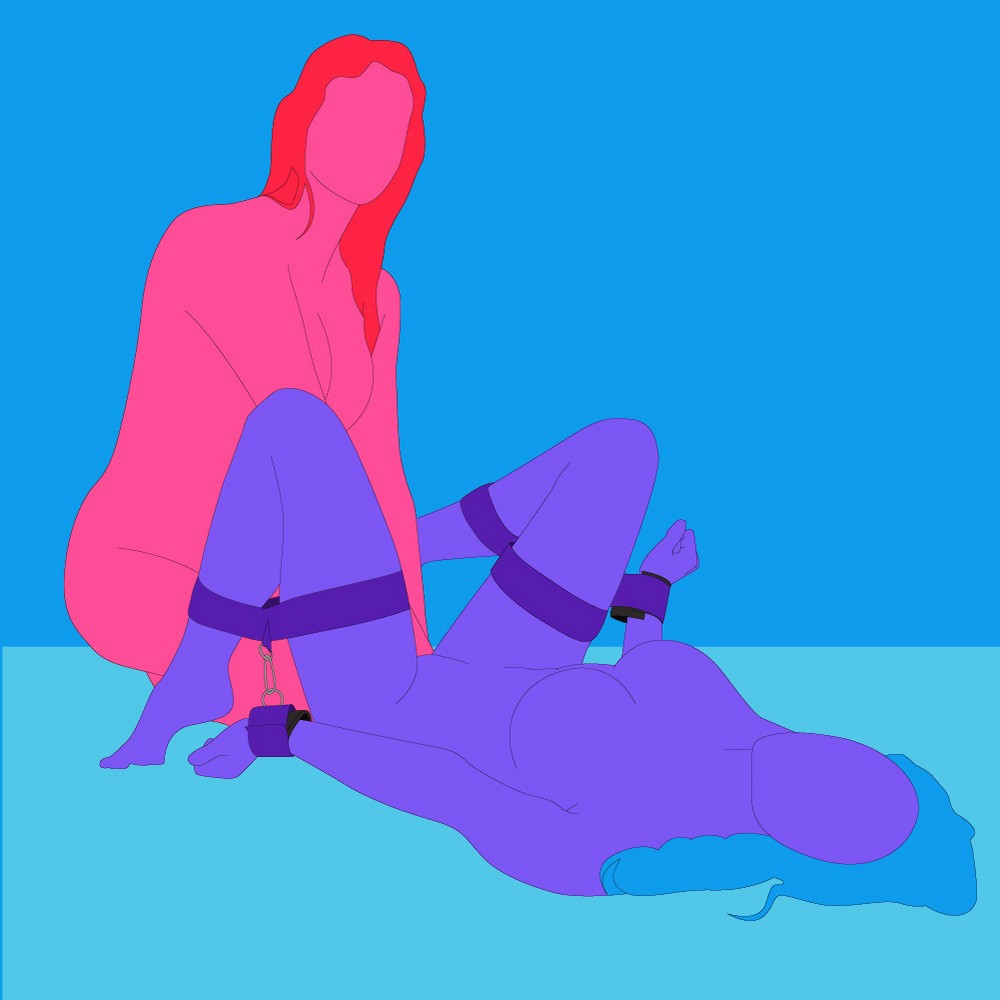 A naked illustrated couple, one is lying on the floor with legs bent, wearing Purple Reins restraints. The other is sat on the floor by their legs.
