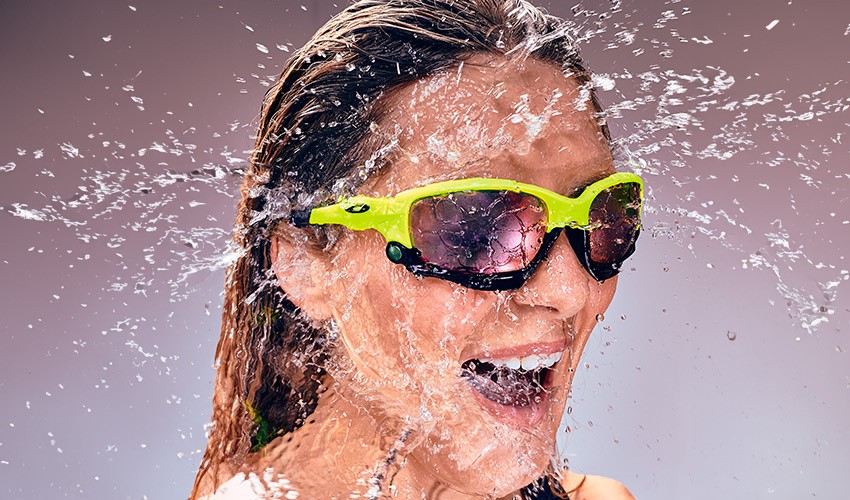 Amelia, co-founder of SULT, is smiling wearing reflective glasses while being splashed with water. 